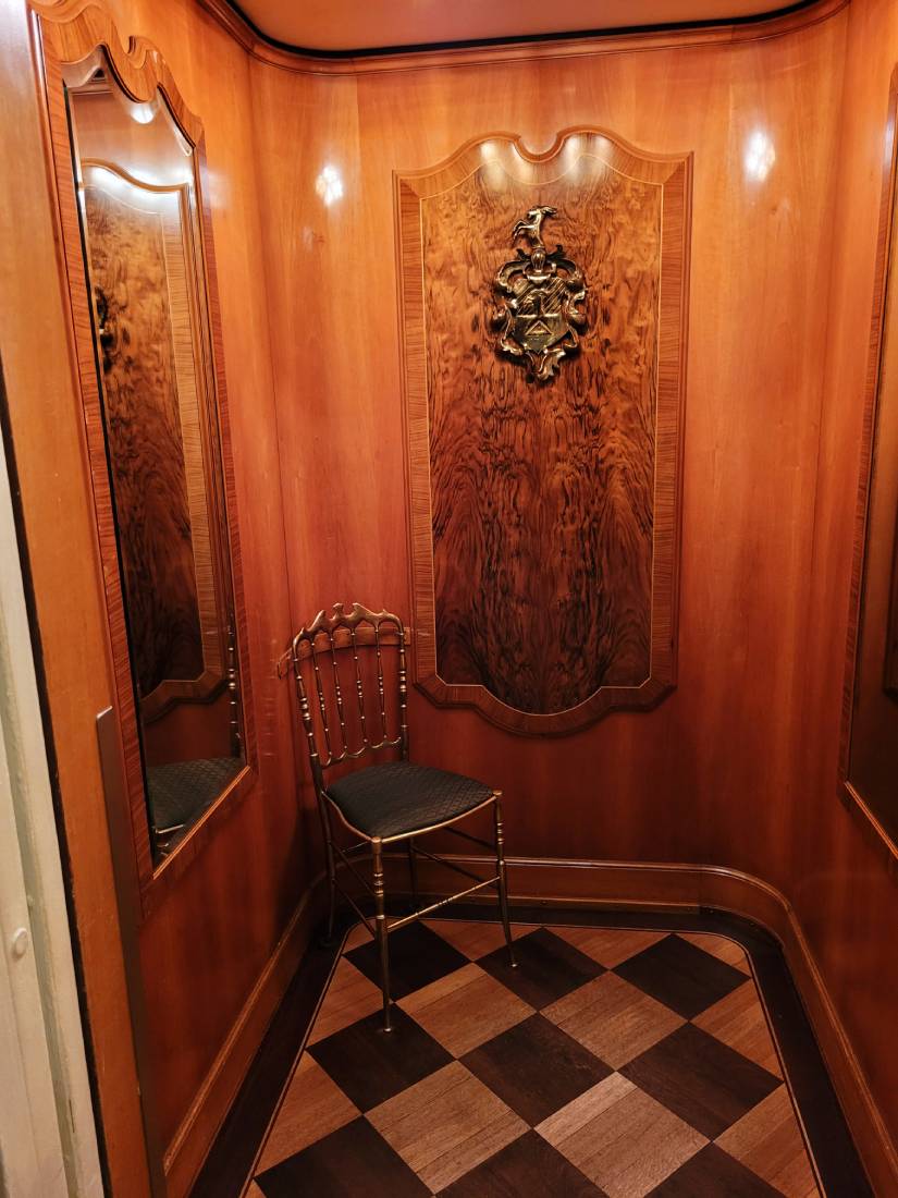 Fahrstuhl innen mit Holzwaenden, kariertem Boden und Stuhl