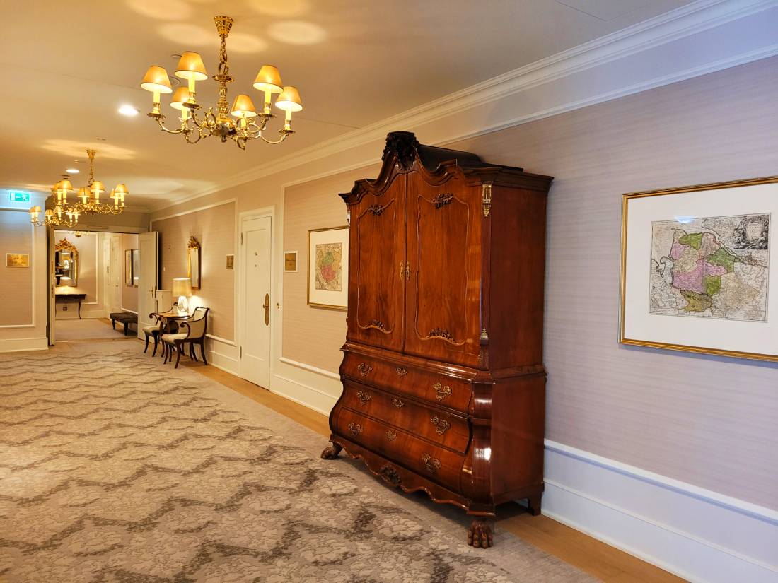 Hotelflur mit antikem brauen Holzschrank, Kronleuchtern, heller gemusterter Teppich